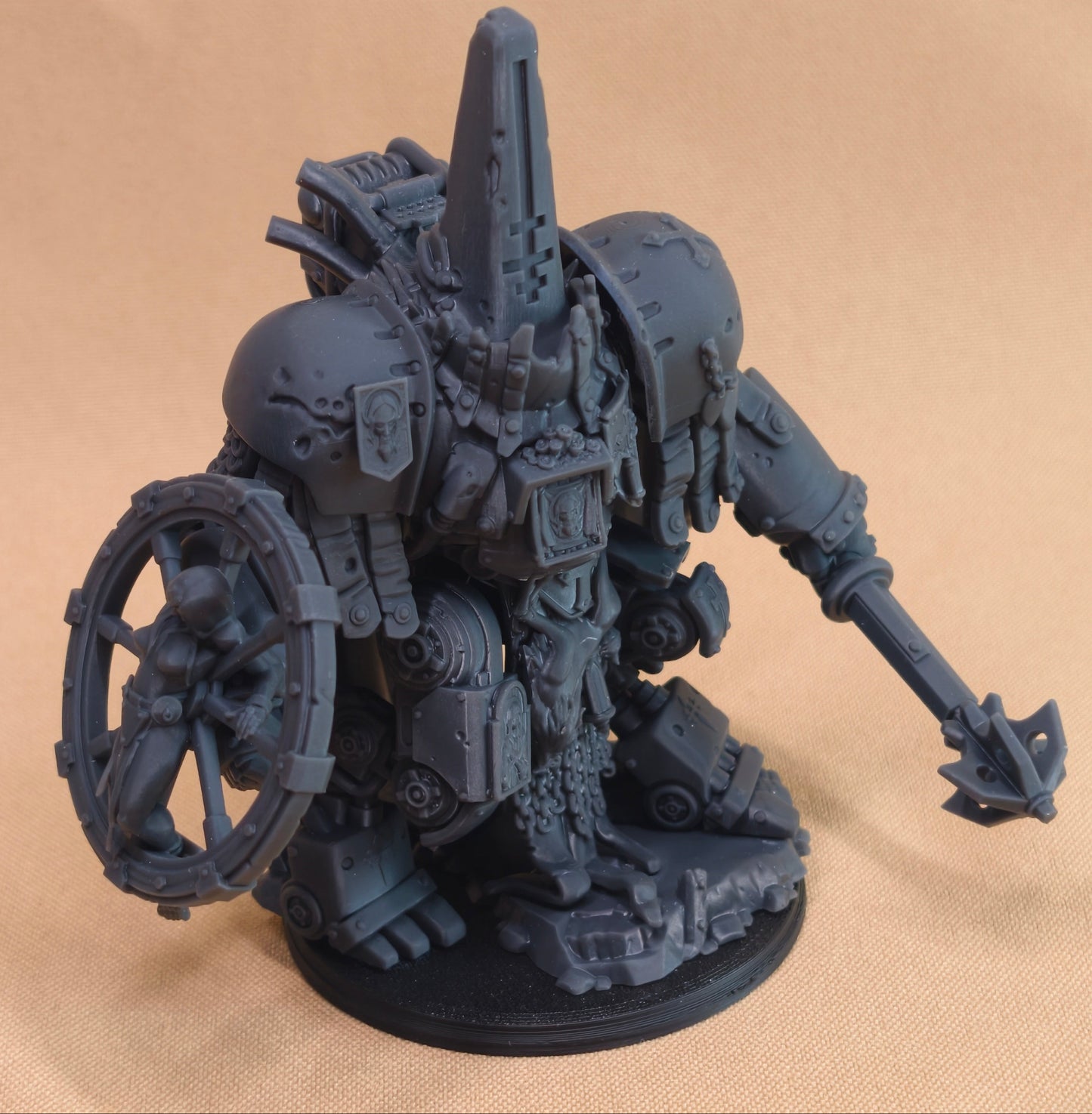 A dark gray unpainted miniature figurine of a heavily armored sci-fi mechanical warrior holding a large shield on one side and a long weapon in the other hand, standing on a round black base